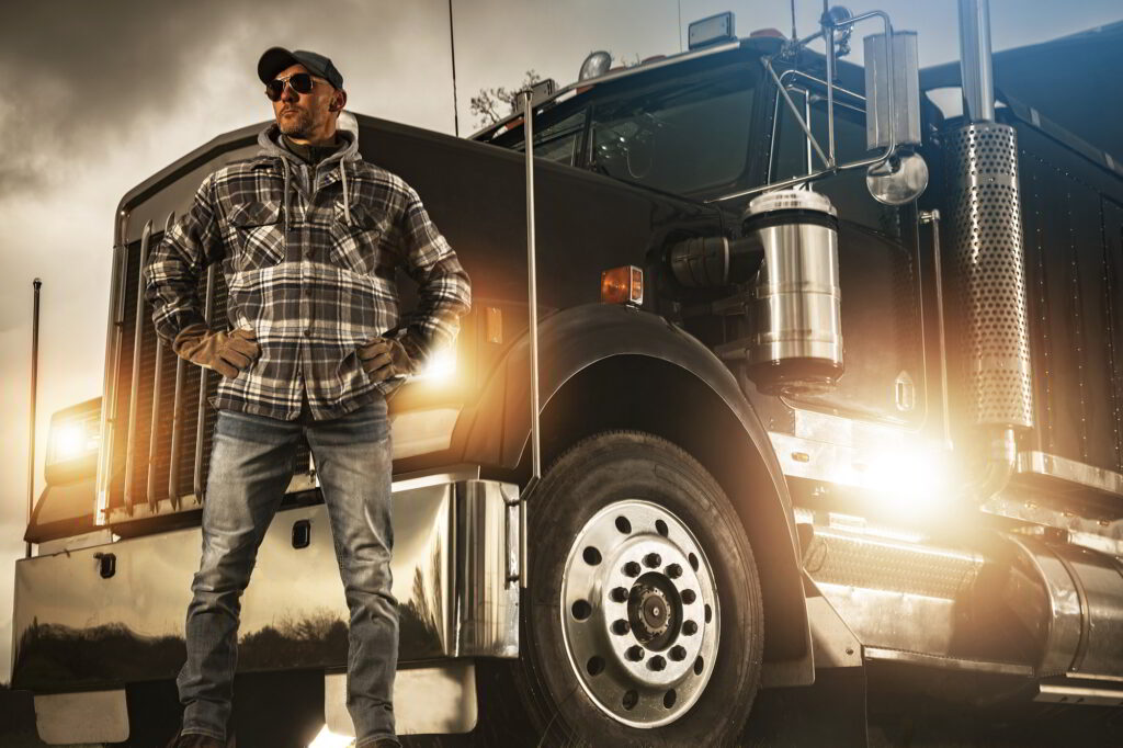 A professional truck driver stands proudly in front of his truck