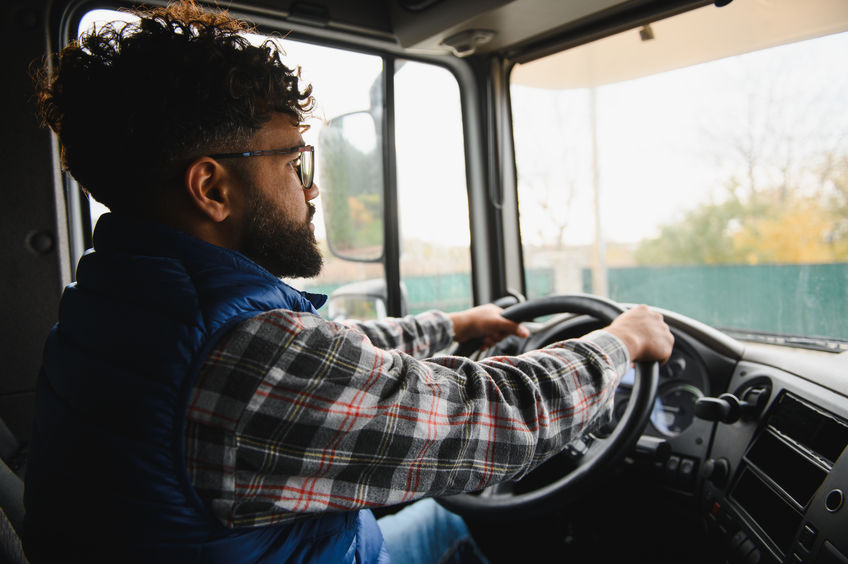 Man with beard and glasses driving a semi truck, focusing on the road ahead. Transporting goods for logistics
